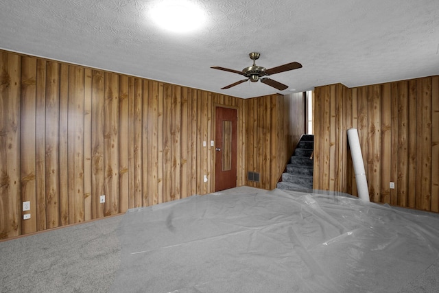 spare room with ceiling fan, wood walls, and a textured ceiling