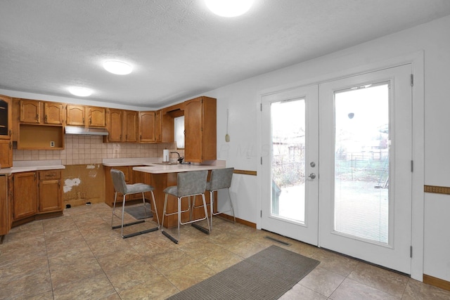 kitchen with backsplash, french doors, a kitchen breakfast bar, a textured ceiling, and kitchen peninsula