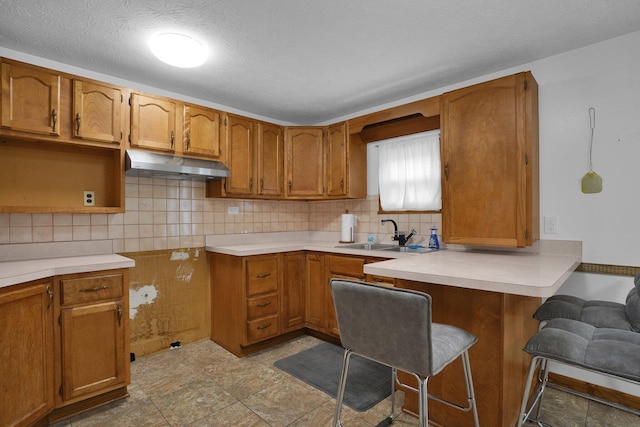 kitchen with a kitchen breakfast bar, backsplash, a textured ceiling, sink, and light tile patterned floors