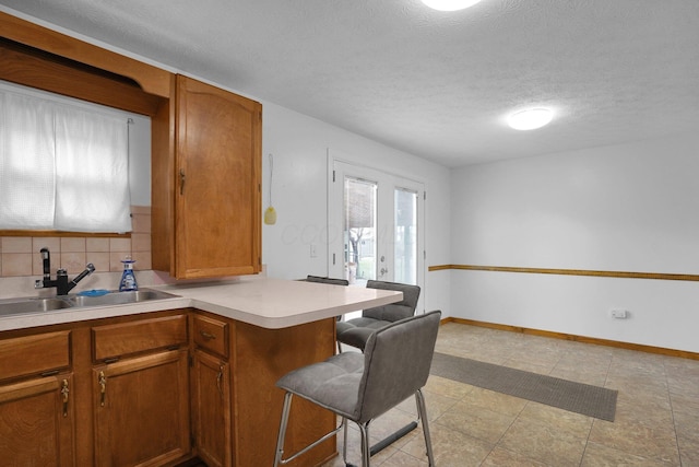 kitchen with french doors, sink, a textured ceiling, tasteful backsplash, and kitchen peninsula