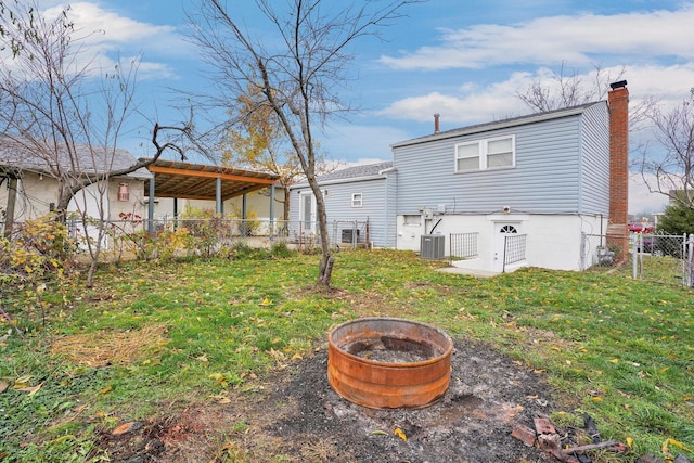 rear view of property with central AC unit, an outdoor fire pit, and a lawn