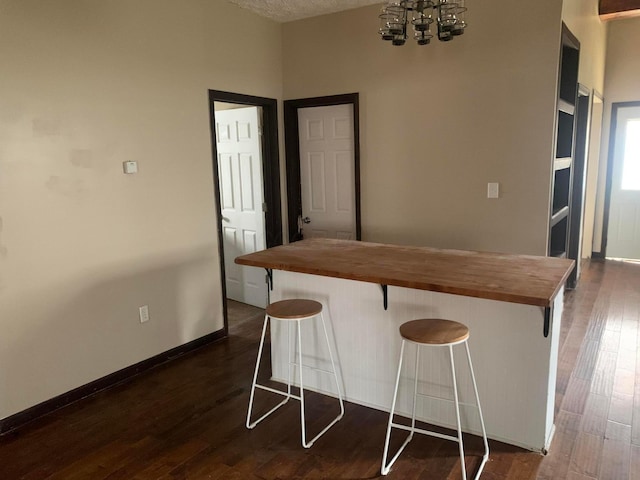 kitchen featuring a kitchen breakfast bar, dark wood-type flooring, wooden counters, and a textured ceiling