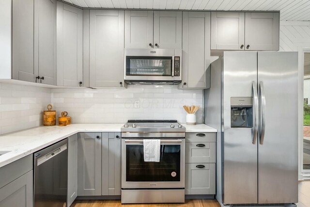 kitchen with tasteful backsplash, gray cabinetry, light stone counters, and appliances with stainless steel finishes