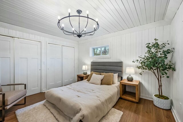 bedroom with hardwood / wood-style floors, an inviting chandelier, wooden ceiling, and wood walls