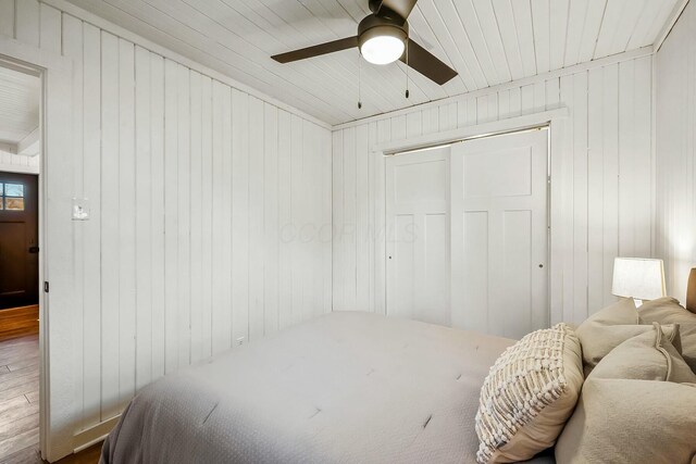 bedroom with hardwood / wood-style floors, a closet, ceiling fan, and wooden walls