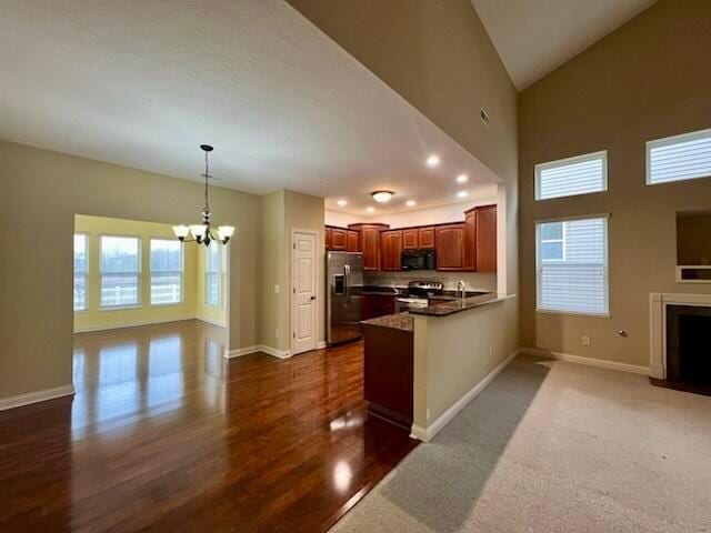 kitchen featuring an inviting chandelier, high vaulted ceiling, kitchen peninsula, pendant lighting, and stainless steel appliances