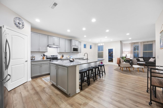 kitchen with gray cabinetry, an island with sink, appliances with stainless steel finishes, and light hardwood / wood-style flooring