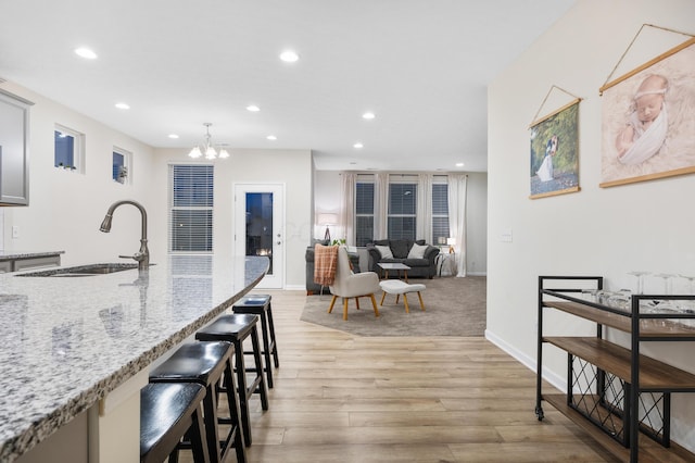 kitchen with a kitchen breakfast bar, sink, hanging light fixtures, light hardwood / wood-style flooring, and light stone counters