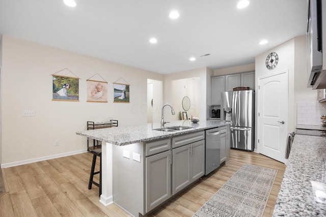 kitchen featuring gray cabinetry, a kitchen island with sink, sink, light wood-type flooring, and appliances with stainless steel finishes