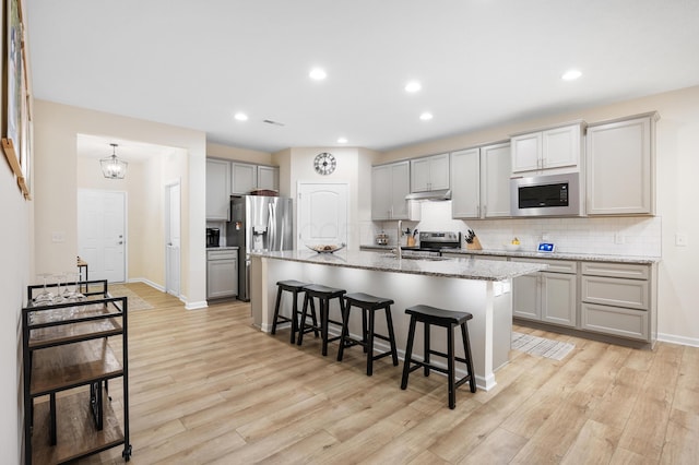 kitchen featuring a kitchen bar, light wood-type flooring, stainless steel appliances, and gray cabinets