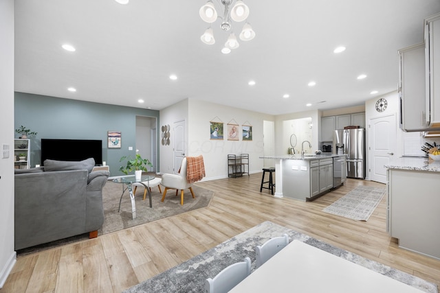 living room with a notable chandelier, light wood-type flooring, and sink