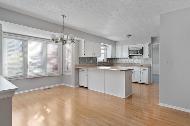 kitchen featuring kitchen peninsula, hanging light fixtures, white cabinets, and a healthy amount of sunlight