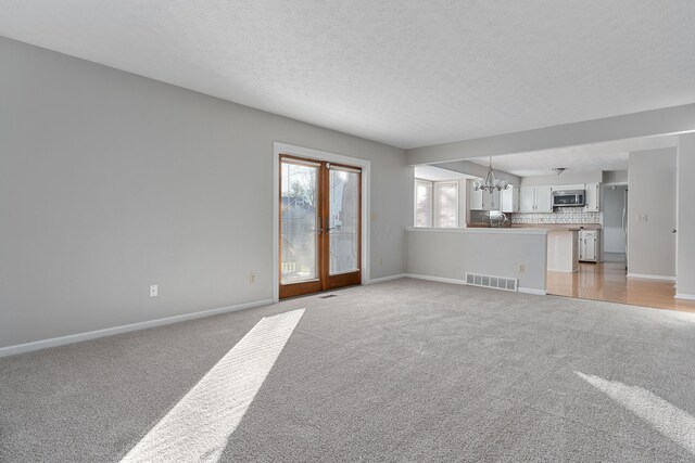 unfurnished living room with light colored carpet, french doors, a textured ceiling, and an inviting chandelier