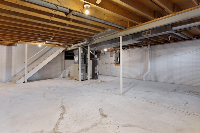 basement featuring heating unit, water heater, electric panel, and brick wall