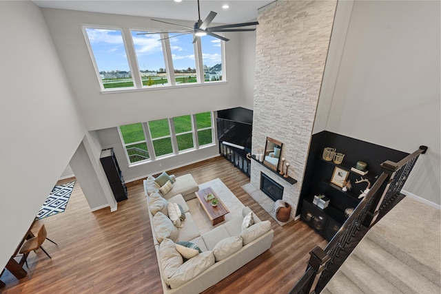 living room featuring a stone fireplace, ceiling fan, and wood-type flooring