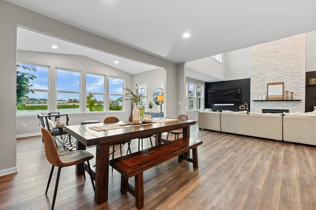 dining room featuring hardwood / wood-style flooring, a stone fireplace, a water view, and vaulted ceiling