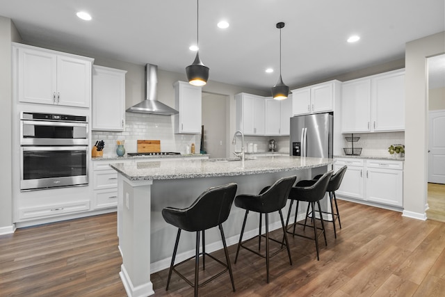 kitchen with hardwood / wood-style floors, stainless steel appliances, white cabinetry, and wall chimney range hood