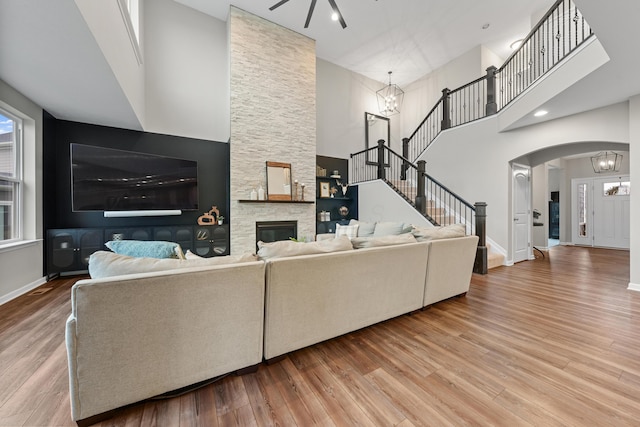 living room with a high ceiling, a stone fireplace, a notable chandelier, and wood-type flooring