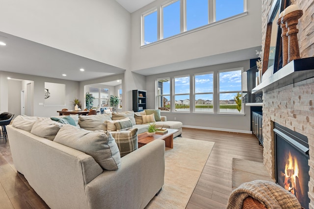 living room with a towering ceiling, light wood-type flooring, and a stone fireplace