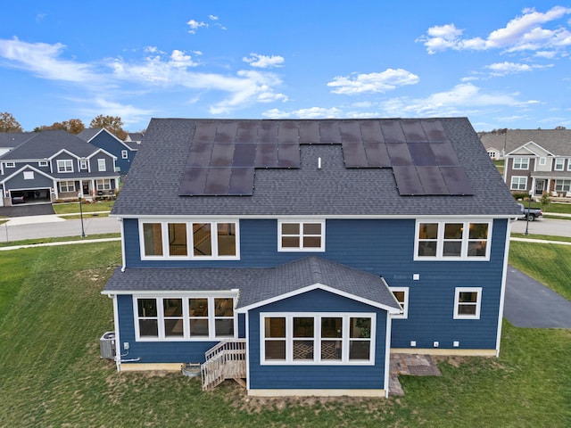 rear view of house featuring central air condition unit, a yard, and solar panels