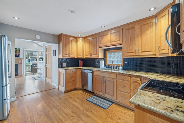 kitchen with sink, light stone counters, decorative backsplash, appliances with stainless steel finishes, and light wood-type flooring