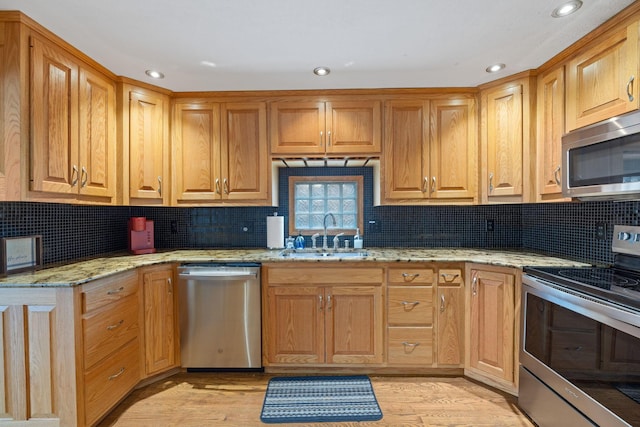 kitchen with appliances with stainless steel finishes, light stone counters, light hardwood / wood-style flooring, and sink