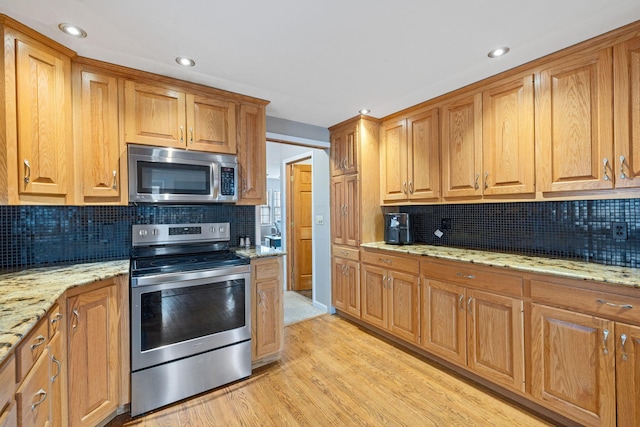 kitchen featuring light stone countertops, appliances with stainless steel finishes, light wood-type flooring, and decorative backsplash