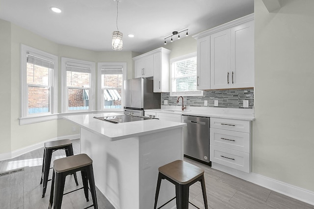 kitchen with sink, appliances with stainless steel finishes, a kitchen island, white cabinetry, and a breakfast bar area