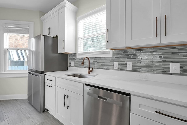 kitchen featuring light stone countertops, appliances with stainless steel finishes, backsplash, sink, and white cabinets