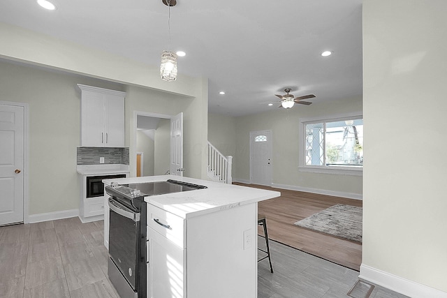 kitchen featuring black range with electric stovetop, white cabinetry, ceiling fan, a kitchen breakfast bar, and light wood-type flooring