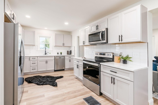 kitchen with appliances with stainless steel finishes, backsplash, light hardwood / wood-style flooring, and white cabinetry