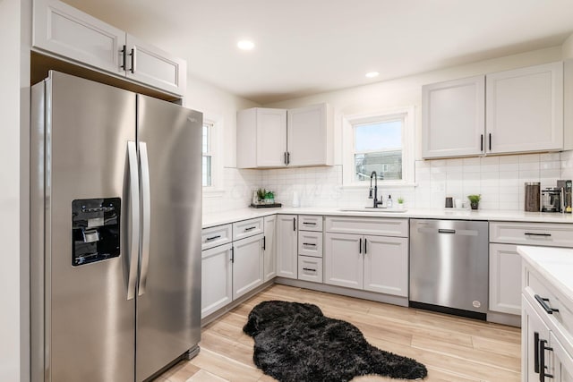 kitchen with appliances with stainless steel finishes, light wood-type flooring, white cabinetry, and sink