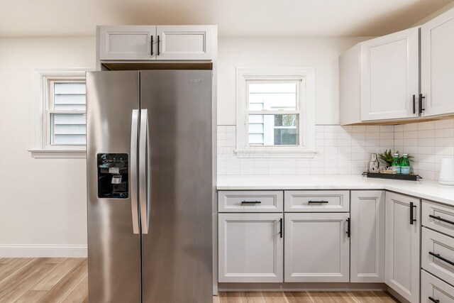 kitchen featuring backsplash, white cabinets, light hardwood / wood-style flooring, light stone countertops, and stainless steel fridge with ice dispenser