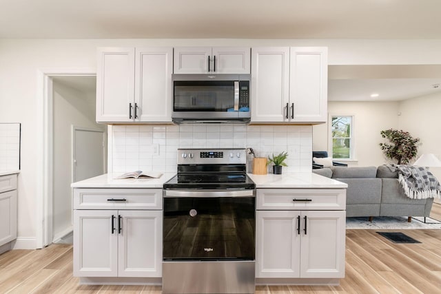 kitchen with backsplash, white cabinets, stainless steel appliances, and light wood-type flooring