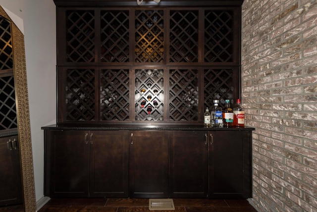 wine room with dark tile patterned floors, brick wall, and bar area