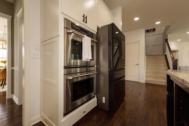 kitchen featuring light stone countertops, black fridge, stainless steel double oven, dark wood-type flooring, and white cabinetry