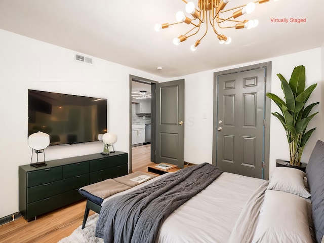 bedroom with a chandelier, connected bathroom, and light hardwood / wood-style floors