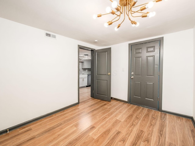 unfurnished bedroom with an inviting chandelier and light wood-type flooring