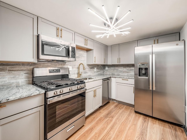 kitchen featuring light stone countertops, light wood-type flooring, tasteful backsplash, stainless steel appliances, and sink