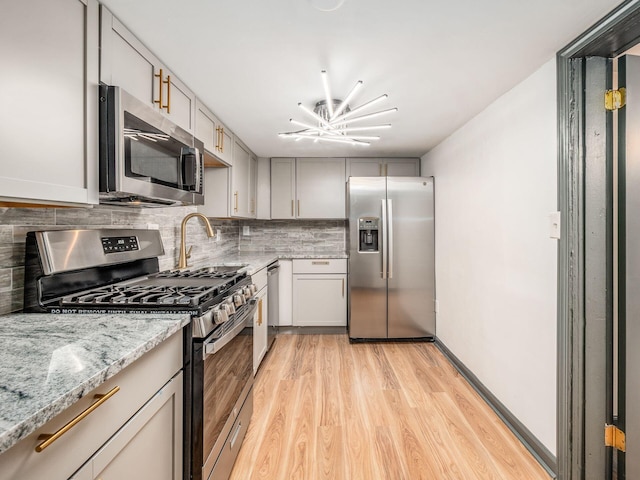 kitchen with decorative backsplash, appliances with stainless steel finishes, light hardwood / wood-style flooring, and light stone countertops