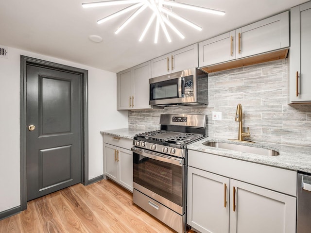 kitchen featuring light wood-type flooring, backsplash, light stone counters, stainless steel appliances, and sink