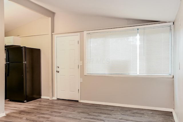 interior space featuring white cabinets, lofted ceiling with beams, black refrigerator, and light wood-type flooring