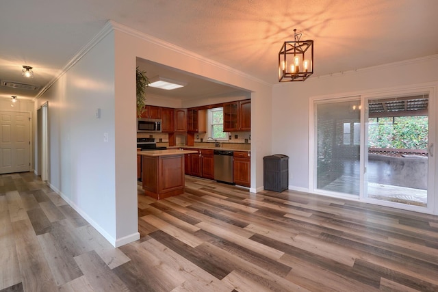 kitchen with appliances with stainless steel finishes, decorative light fixtures, a kitchen island, and a wealth of natural light