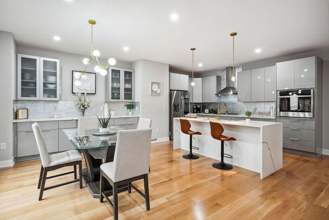 kitchen with wall chimney range hood, pendant lighting, stainless steel appliances, and an island with sink