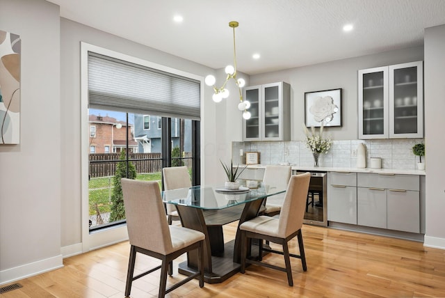 dining area with a notable chandelier, light hardwood / wood-style floors, a textured ceiling, and beverage cooler