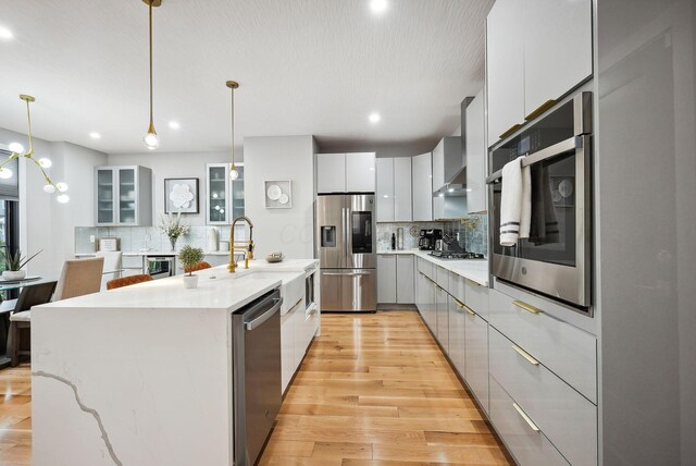 kitchen featuring white cabinets, a large island with sink, stainless steel appliances, and hanging light fixtures