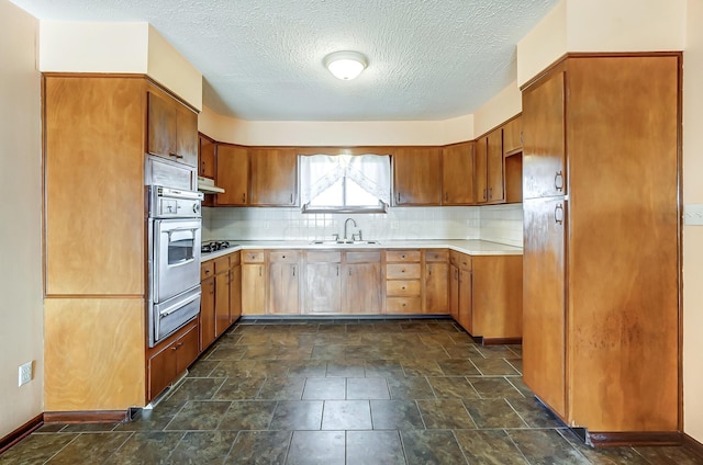 kitchen with tasteful backsplash, sink, oven, and a textured ceiling