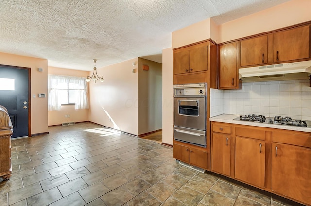 kitchen with pendant lighting, a textured ceiling, appliances with stainless steel finishes, tasteful backsplash, and a notable chandelier