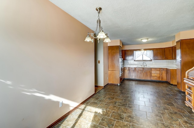 kitchen with tasteful backsplash, stainless steel oven, sink, decorative light fixtures, and a chandelier