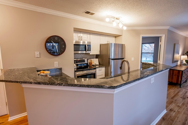 39 Buttles Ave Unit 39, Columbus, OH 43215 - kitchen featuring appliances with stainless steel finishes, white cabinetry, wood finished floors, tasteful backsplash, and ornamental molding